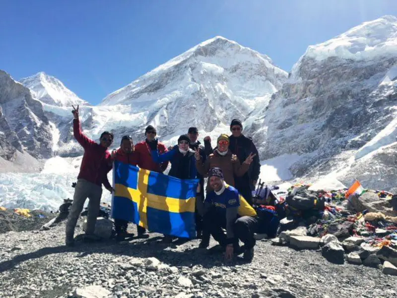 Glada vandrare upp på Mount Everest Base Camp. Berg och blå himmel i bakgrunden.